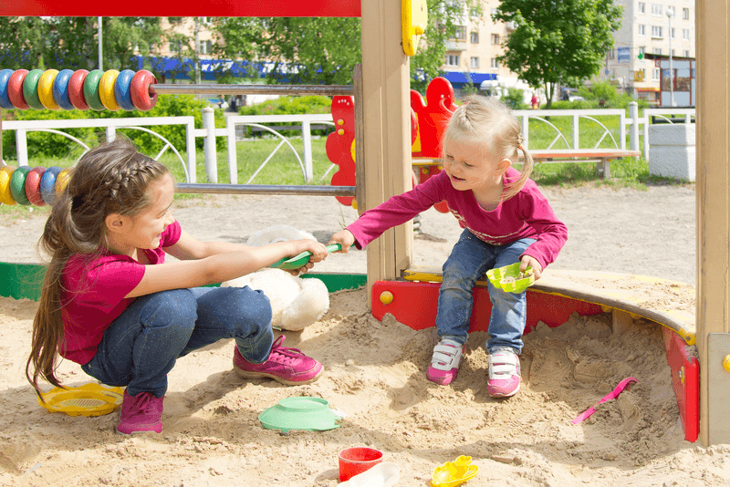 Twee kinderen trekken in de zandbak aan een schepje