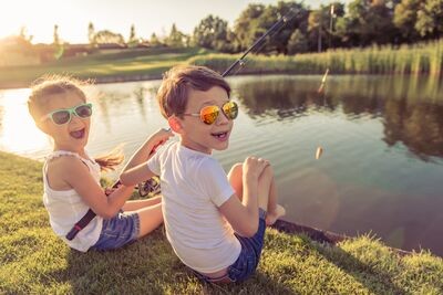 Twee kinderen zijn aan het vissen en kijken lachend naar de camera