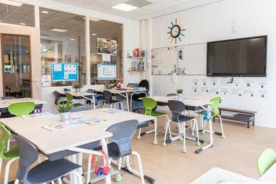 Foto van een klaslokaal met lege bureaus en stoelen en een groot scherm aan de muur